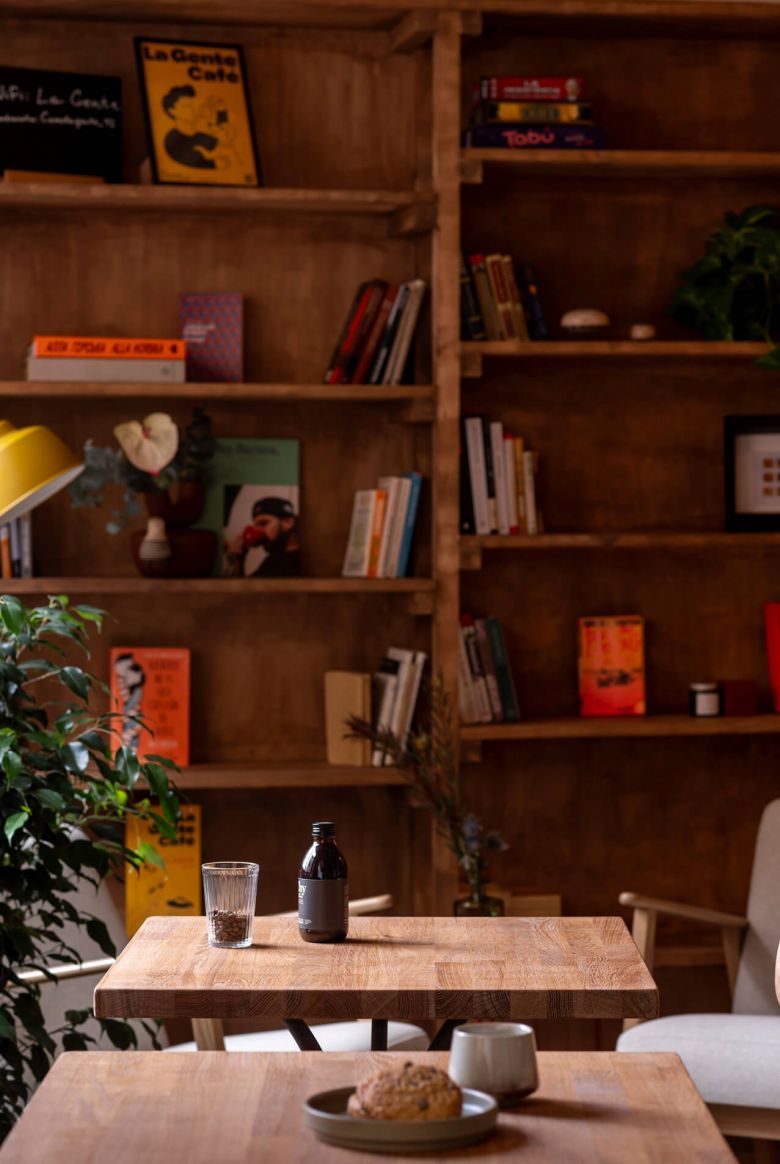 A woman sits at a table in La Gente Cafe, with a book open in front of her, designed by TenZeroTwo Bureau